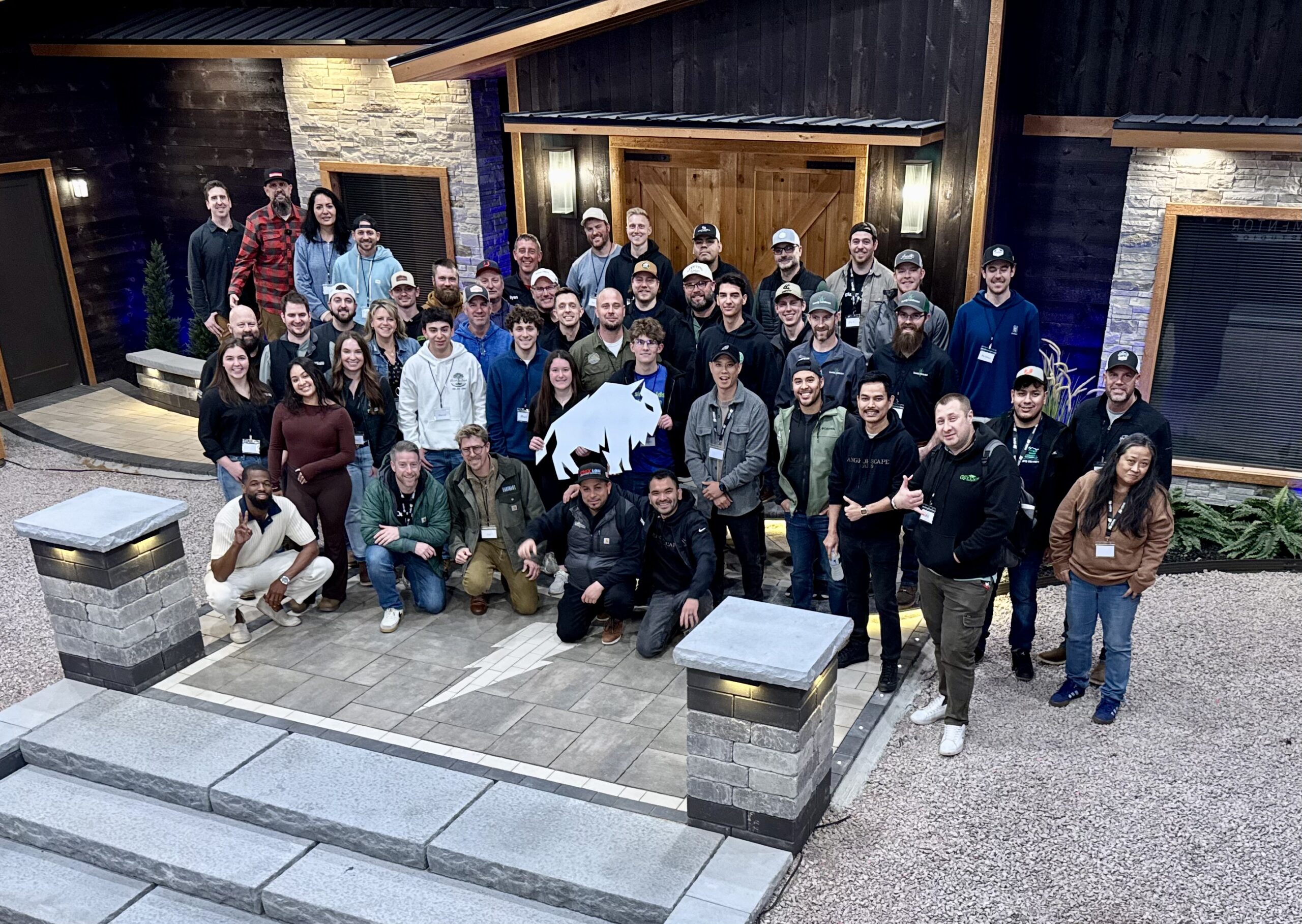 Group of hardscape contractors and industry professionals gathered at a Hardscape Mentor design lab featuring paver installations, stone columns, steps, walls, and landscape lighting.